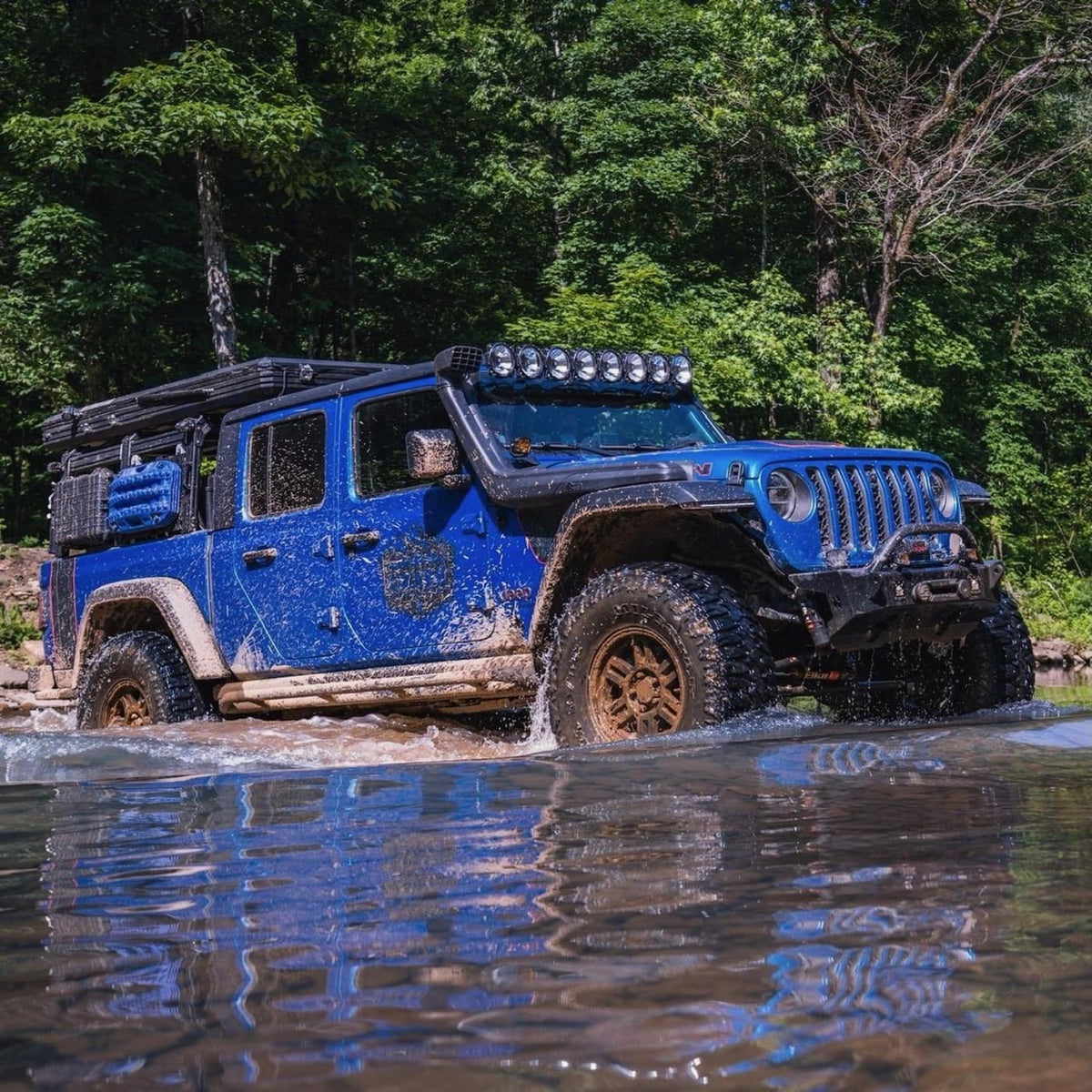 Blue Jeep Gladiator splashing through a creek on the trail